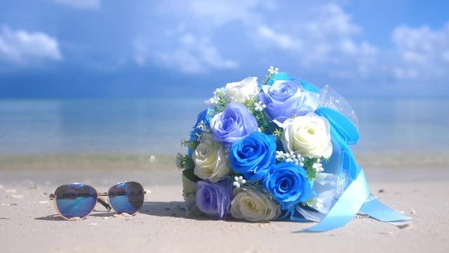 Bouquet beautiful flowers and sunglasses on the beach white sand tropical paradise island on sea water ocean background and cloudy sky changes focus to the sea. slow motion. 3840x2160. 4k