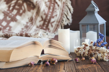 Details of still life in the home interior living room. Beautiful tea Cup, cut wood, books and pillows, candle on wooden background. Vintage, rustic. Cosy autumn-winter concept