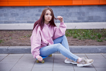 Cheerful young woman in sunglasses sitting on skateboard and having fun over pink background