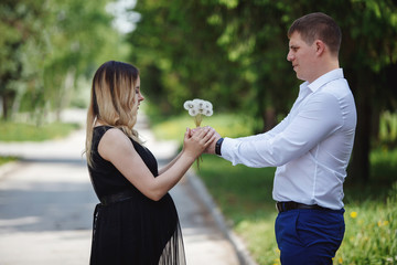 Young handsome guy gives a bouquet of flowers to his pregnant wife in a blooming apple orchard.