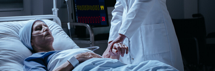 Close-up of a doctor checking pulse of his dying of cancer patient in the hospital