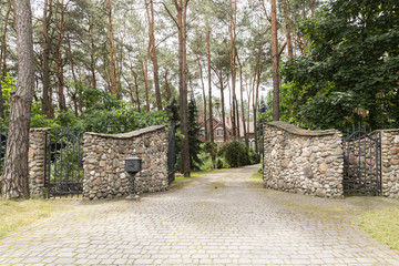 Stone gate and driveway to residence in the forest. Real photo