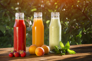 Bottles with juice and fruits on a green background, food concept. Summer, sunlight