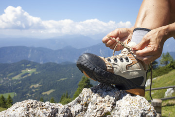 Hiker tying boot laces on rock, high in the mountains, space for text