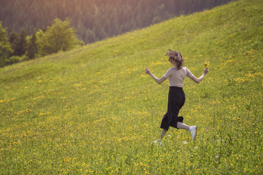 Girl with a bouquet is running on the flower meadow. Sunny summer day