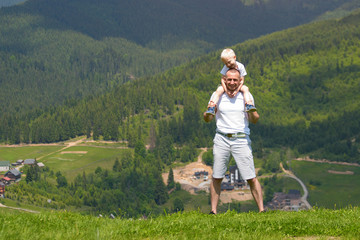 Fototapeta na wymiar Father with a small son on his shoulders. Mountains on the background. Summer sunny day.