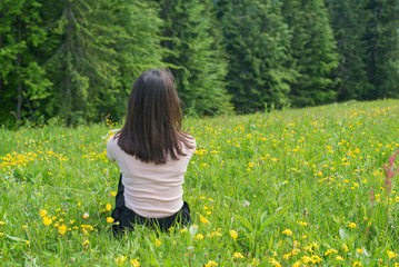 Fototapeta premium Girl sits on a green lawn near a forest. Back view