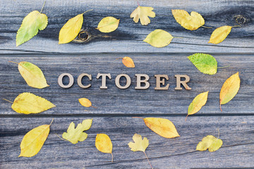 Naklejka premium Inscription October on a wooden background, frame of yellow leaves
