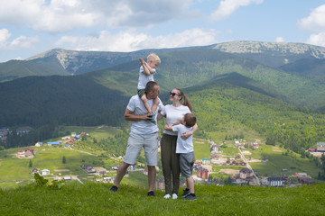 Fototapeta na wymiar Family holiday. Parents and two sons admire views of the valley. Mountains in the distance. Back view
