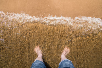 Men's feet in the water at the sandy shore