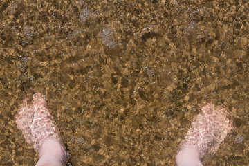 Men's feet in the water at the sandy shore