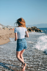 Young girl runs along the sea sandy beach barefoot, concept, view from behind.