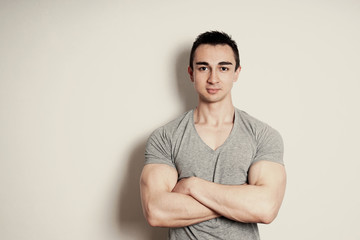 muscular young man with arms crossed standing against wall with copy space. vintage filter effect.