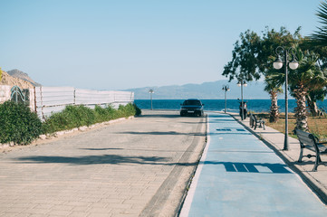 On the embankment in the shade of palm trees there is a black car on the background of the sea and...