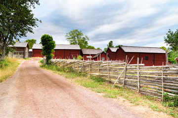 Country road with roundpole fences on the sides. Village barns in the background. Location Stensjo in Smaland, Sweden. © imfotograf
