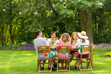 Friends laughing, sitting at a garden table, eating a vegetarian meal and telling jokes