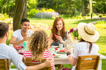 Happy group of teenagers eating watermelon and having fun during an outdoor party