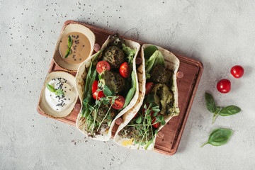 top view of falafel with tortillas, cherry tomatoes and germinated seeds of sunflower served on wooden board on grey surface