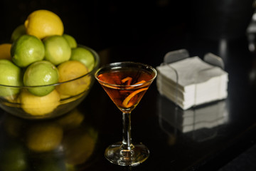 Closeup glass of Manhattan cocktail decorated with orange twist at bar counter background.