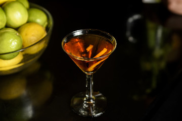 Closeup glass of Manhattan cocktail decorated with orange twist at bar counter background.