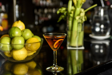 Closeup glass of Manhattan cocktail decorated with orange twist at bar counter background.
