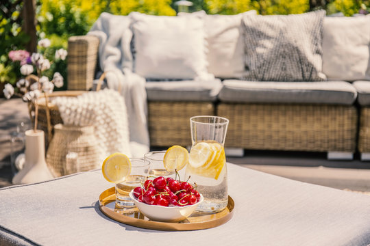 Fruits and glass with water on rattan table on the terrace with settee and flowers. Real photo
