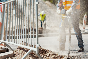 Close-up of a pneumatic hammer held by a worker and dust in the air at roadworks - obrazy, fototapety, plakaty