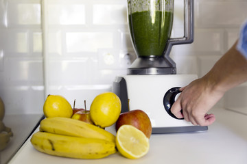 Woman blending spinach, bananas, lemon and apples to make a healthy green smoothie. Healthy living concept 