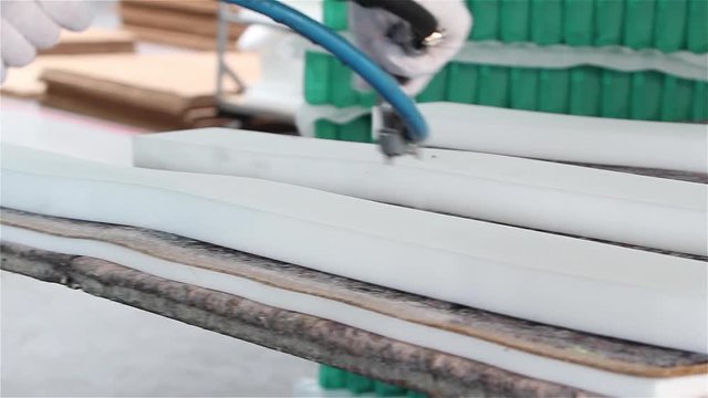 Factory on assembly of orthopedic mattresses, production of mattresses, gluing foam rubber close-up, the worker applies glue on the mattress
