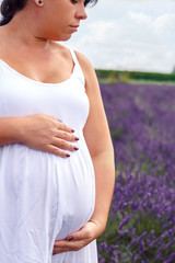 Close up of belly of pregnant girl in a lavender flowers field.