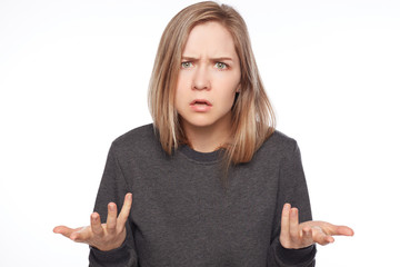 Portrait of furious young Caucasian female gestures in anger, being dissatisfied with results of work, screams loudly. Frustrated blond haired lady full of rage gestures against white studio wall.