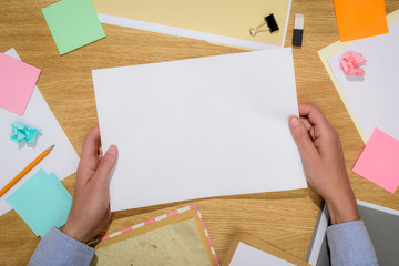 Obraz premium cropped image of woman holding empty white paper over table with stationery supplies