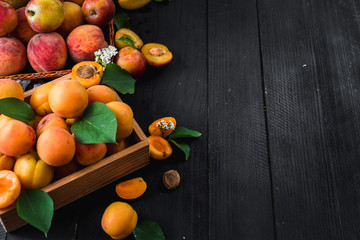 Fresh ripe apricots and plums on black wooden background. Copy space