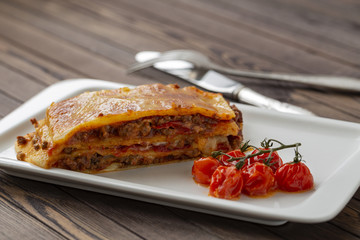 Tasty lasagna with meat covered with cheese, served with baked tomatoes on a white plate.