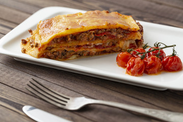 Tasty lasagna with meat covered with cheese, served with baked tomatoes on a white plate.