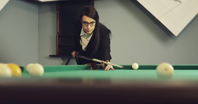 Confident business woman in glasses plays billiards.
