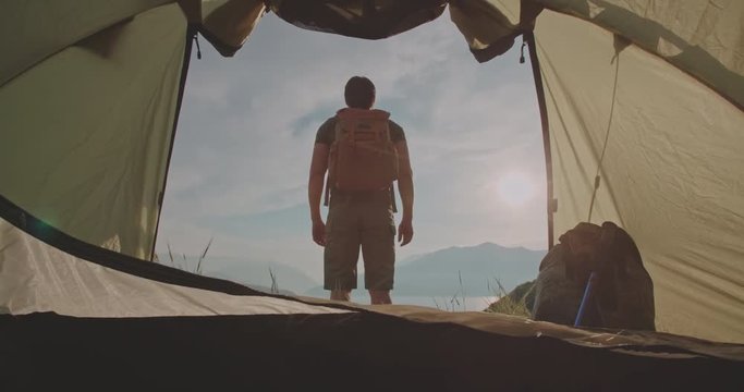 young handsome caucasian man coming out of his tent, enjoying the view of mountains and sky with clouds - zen concept, 4k