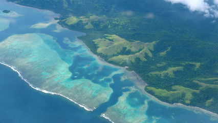 AERIAL: Ocean waves roll over the coral reef and towards the exotic island
