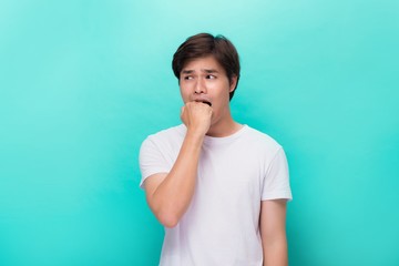 Angry irritated aggressive young bearded man in white t-shirt biting his fist over blue background