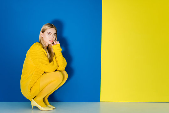 Female Fashion Model In Yellow Outfit Sitting On Blue And Yellow Background