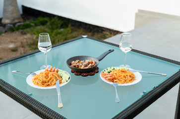 View of delicious and tasty homemade Spanish or Canarias dish, with sea fruits. Healthy dinner outside for two people. Vegetables, Italian pasta with tomato sauce. View of palm tree.