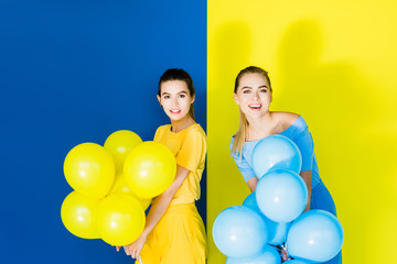 Elegant stylish women smiling and holding party balloons on blue and yellow background
