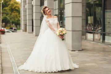 Beautiful bride in luxurious white dress on a city street. In the background the projection of the columns