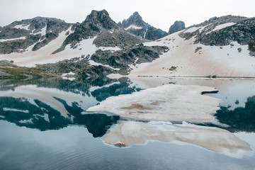 Fototapeta na wymiar ice floe Drifts at mountain cold lake. snowy peaks reflected in water