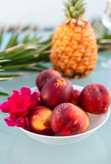View of tasty breakfast on glass table, juice fruits, nectarine, watermelon, pineapple, water and bake. Healthy, colorful and exotic food in paradise. Summertime concept. Palm leaf on background.