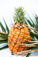 Close up of fresh and tasty little Canarias pineapple among leaf of palm, standing on glasses table. Exotic fruit for breakfast in hotel or resort restaurant. Raw fruit with many vitamins.