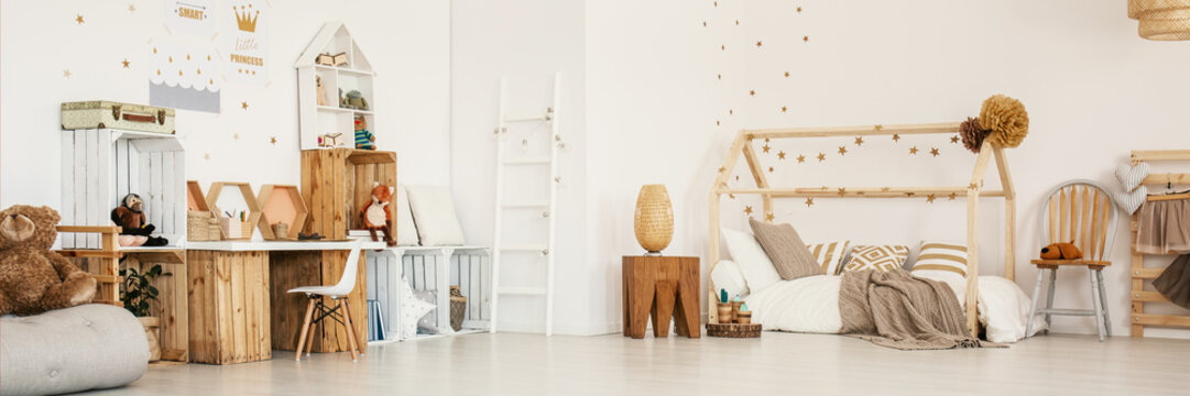 Panoramic photo of a child's bedroom interior with wooden furniture, house bed, stool and wall stickers