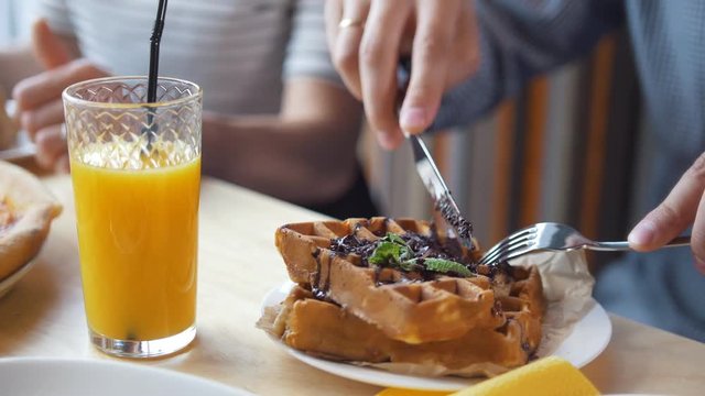 Male hands cuts a yummy belgian waffles with a knife and fork in restaurant