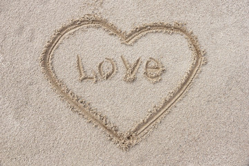 heart drawn on the sand on the beach stick in the center inscription love