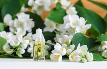 Small glass bottle with natural jasmine roll on perfume oil. Jasmine blossom flowers background....